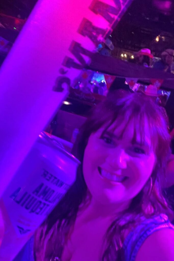 Gemma Lawrence of This Brits Life holding a can of Tequila Paloma, smiling under pink lighting, during the Calgary Stampede after-party at Ranchman's.
