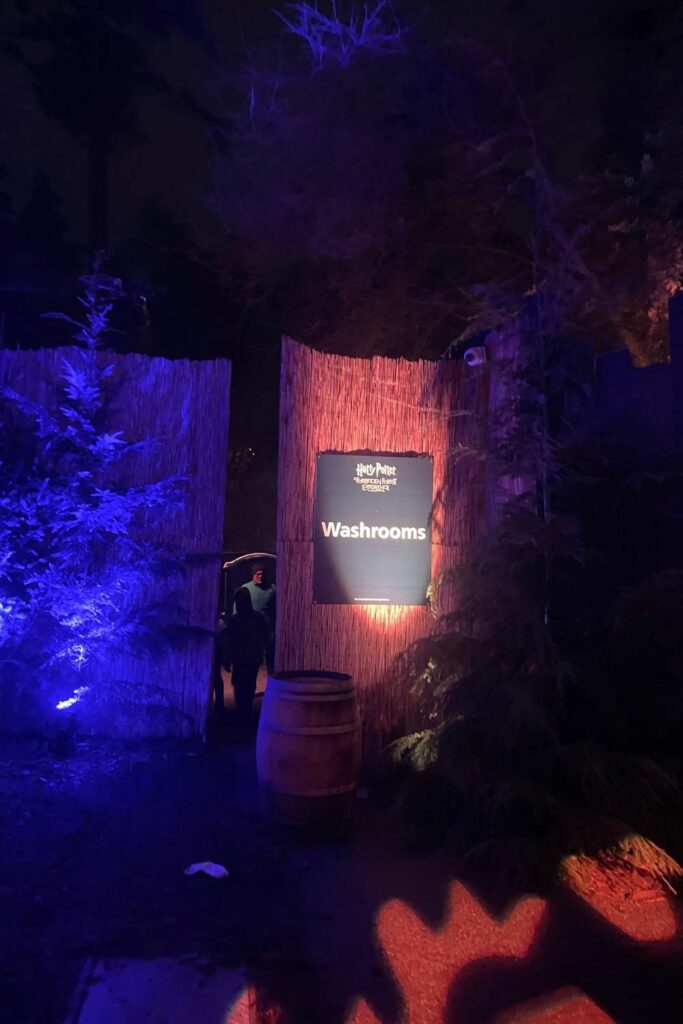 Washrooms sign inside the Harry Potter Forbidden Forest Experience, lit with purple and blue forest lighting.