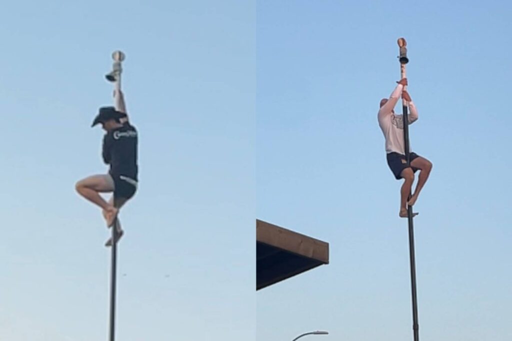 A Cowboy and a Firefighter climbing tall poles on the Ranchman's patio during the Cowboy's versus Firefighters pole climb competition, with clear skies in the background.