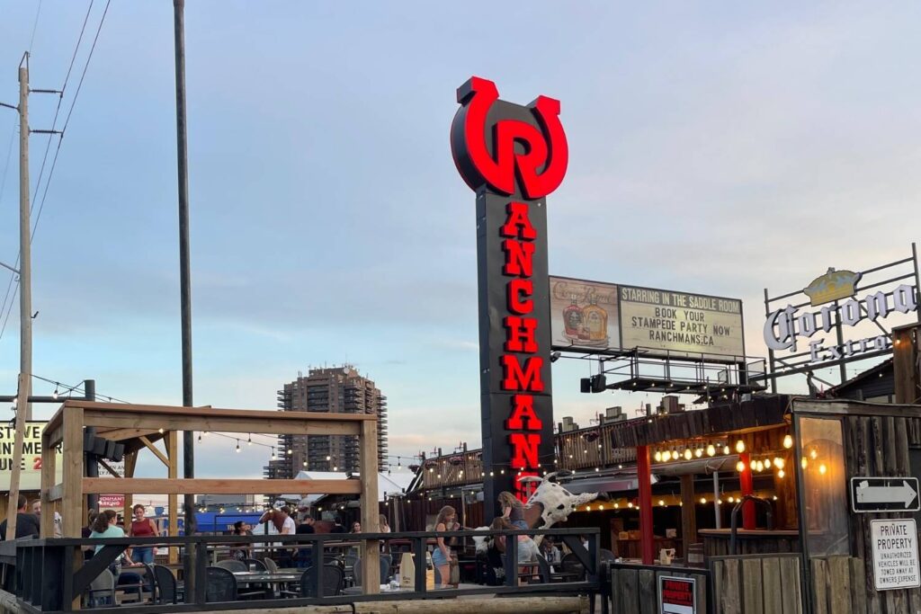 The exterior of Ranchman’s, a western-themed venue, featuring a large red horseshoe-shaped sign with the name “Ranchman’s” prominently displayed, and a Corona Extra sign nearby.