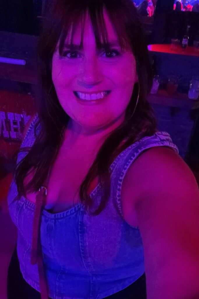 Gemma Lawrence of This Brits Life smiling in a purple-lit room at Ranchman's, dressed in a denim top, with a bar visible in the background.