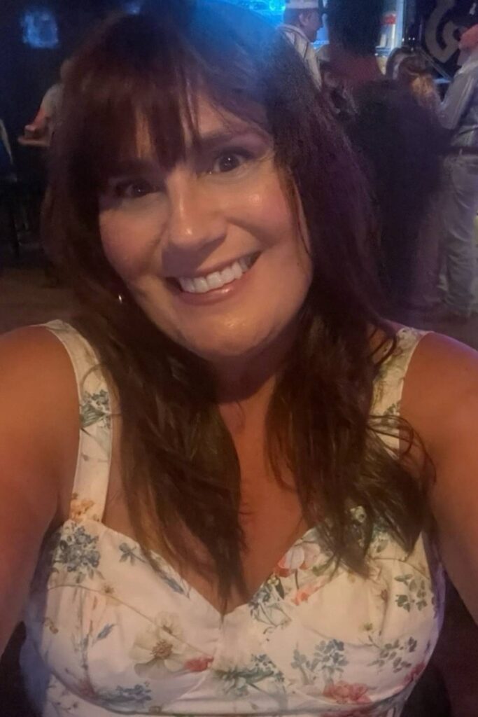 Gemma Lawrence of This Brits Life smiling in a close-up selfie at Ranchman's, with a crowd and blue lighting in the background, dressed in a floral top.