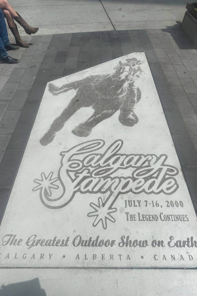 A concrete commemorative floor sign at the Calgary Stampede depicting a rider on a bucking horse with the text "The Greatest Outdoor Show on Earth - Calgary, Alberta, Canada - July 7-16, 2000".