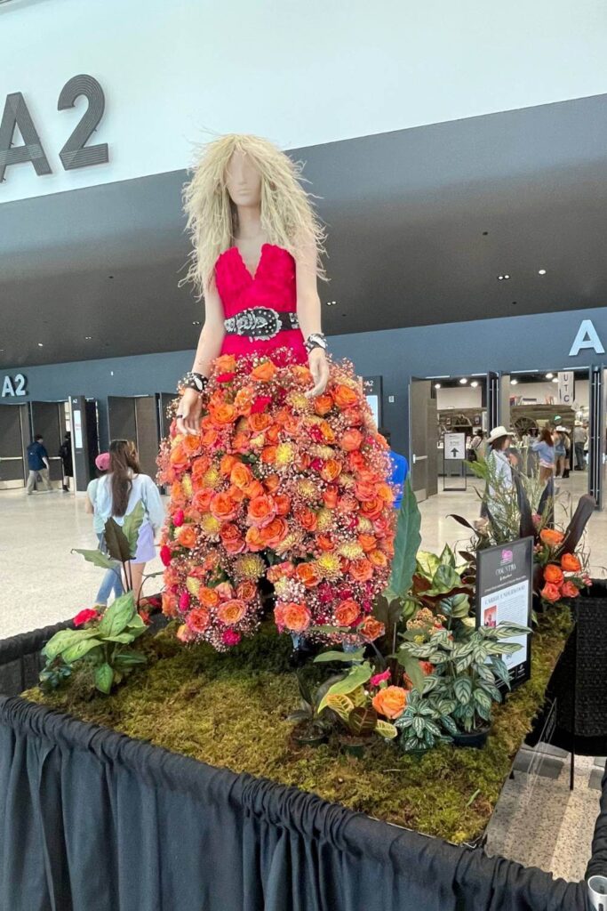 A floral sculpture of Carrie Underwood wearing a vibrant red top with a wide black belt and a voluminous skirt made entirely of orange and pink flowers, displayed inside the BMO Centre during Calgary Stampede.