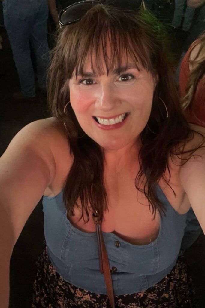 Gemma Lawrence smiling and taking a selfie inside the Nashville North tent during the evening, as her face is illuminated while the background is darker.