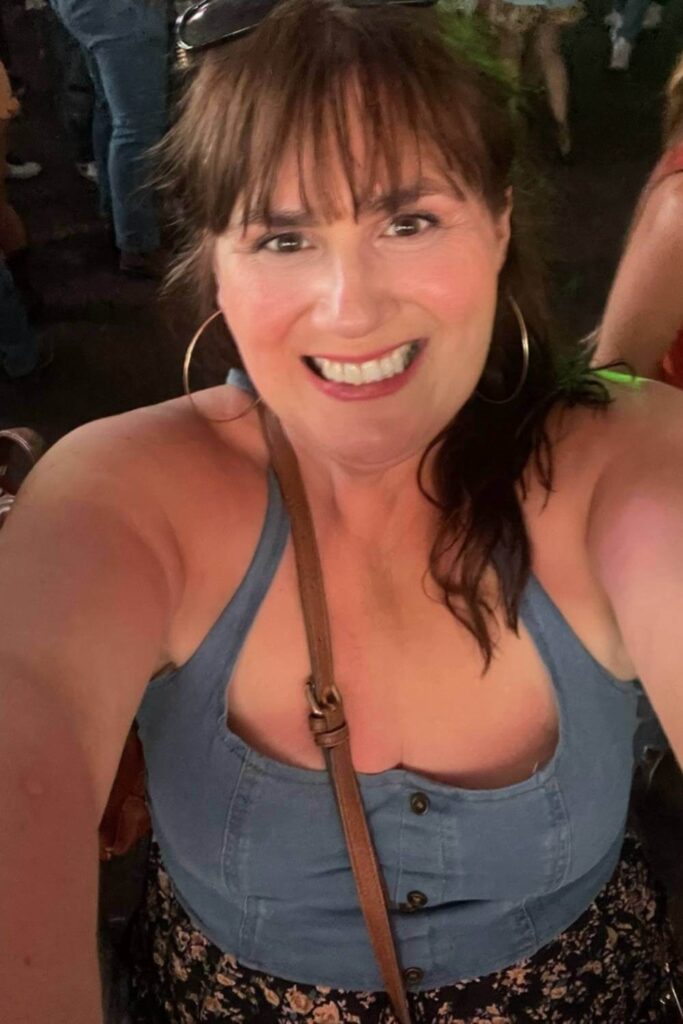 A close-up selfie of Gemma Lawrence with sunglasses perched on her head, taken inside the Nashville North tent during the Calgary Stampede, with a crowd of people and a festive atmosphere visible behind her. 