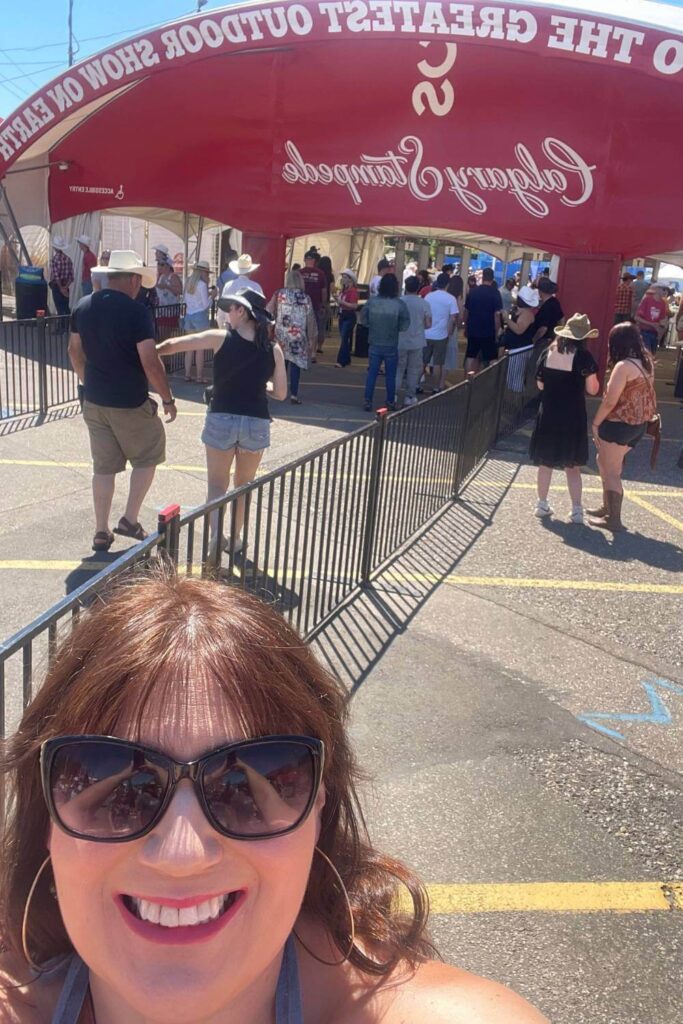 Gemma Lawrence smiling and taking a selfie at the entrance of the Calgary Stampede, with a red archway that reads "Welcome to the Greatest Outdoor Show on Earth" in the background.