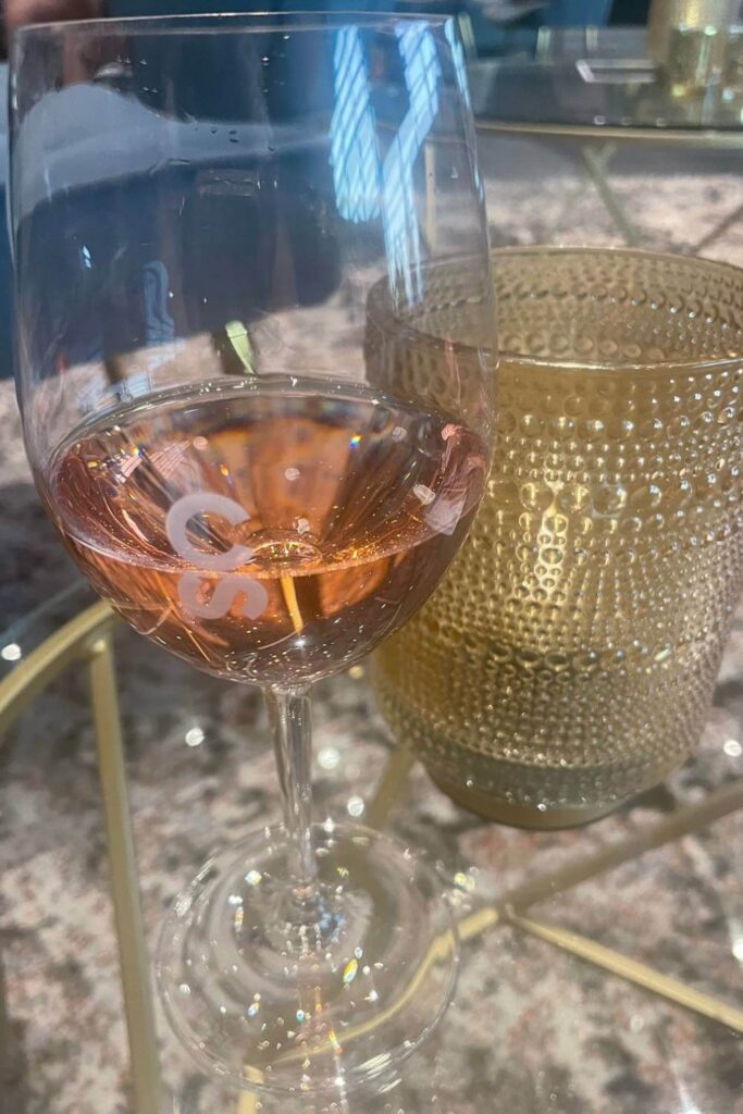 A close-up of a glass of rosé wine with the letters "CS" etched on it, placed next to a decorative glass candle holder, reflecting the upscale atmosphere of the setting.