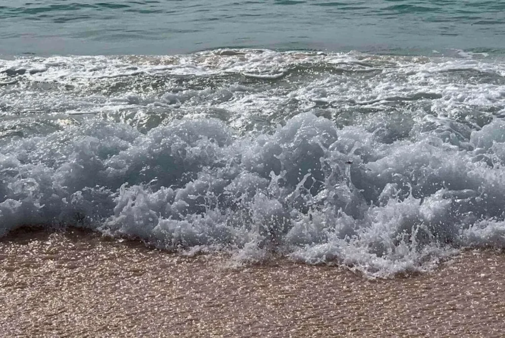 A wave crashes onto the pink sands of Bermuda, capturing the dynamic interaction between the frothy white seafoam and the unique blush-colored beach.