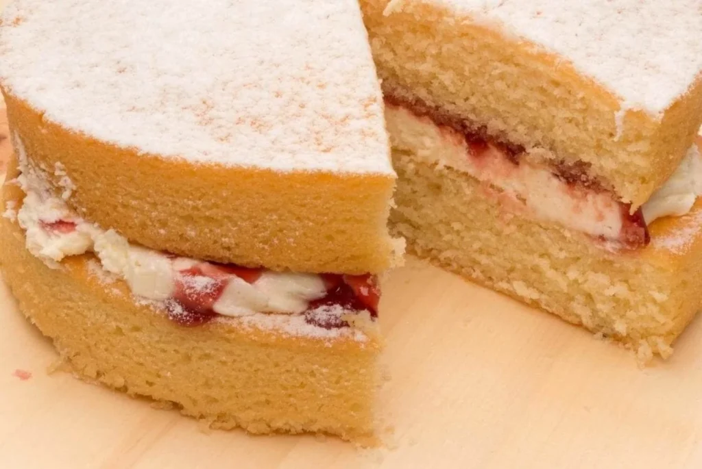 A Victoria sponge cake with a dusting of powdered sugar, featuring layers of whipped cream and strawberry jam.