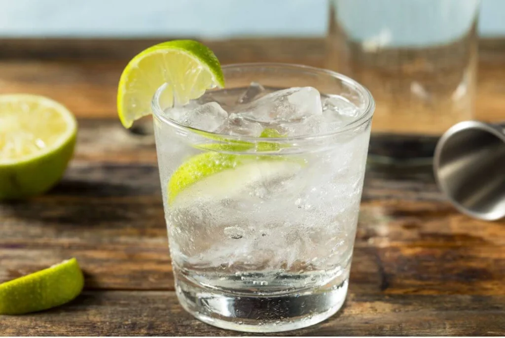 A classic British gin and tonic served with ice and fresh lime in a glass on a rustic wooden table, representing the traditional gin craze and British drinking culture.