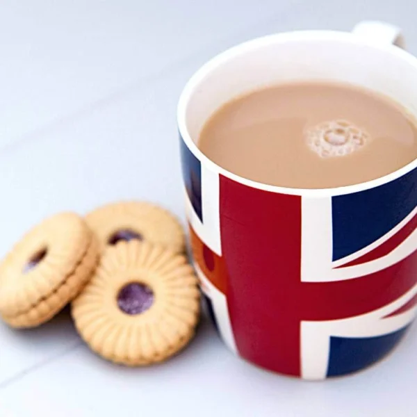 A cup of British tea with milk served in a Union Jack mug beside a few classic British biscuits on a white table, symbolizing traditional British tea culture.