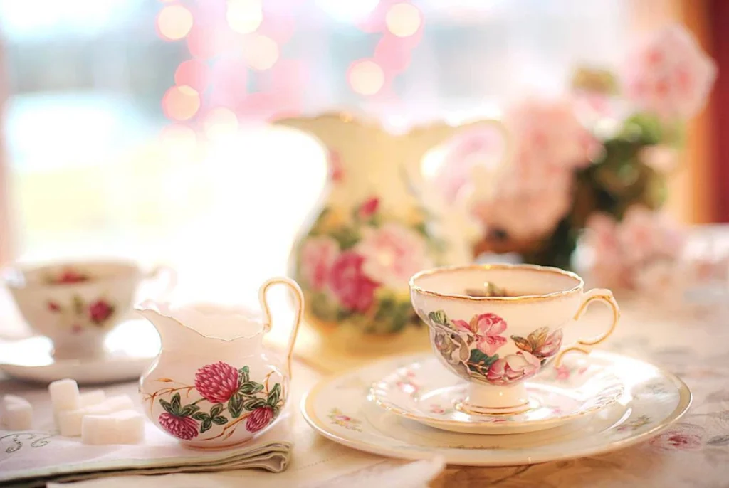 A vintage English afternoon tea setup with floral porcelain teacups, a matching milk jug, sugar cubes, and soft pink flowers in the background, symbolizing classic British tea culture.