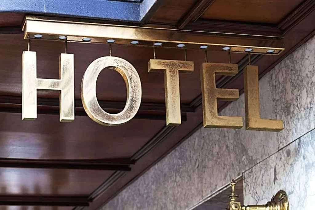Vintage brass 'HOTEL' sign mounted on a wood-paneled wall with a marble backdrop, conveying a sense of classic hospitality and elegance.