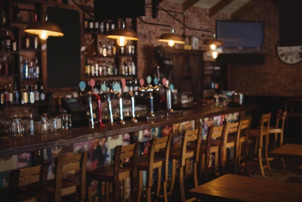 Cozy British pub interior with wooden chairs, beer taps, and warm lighting behind a rustic bar. 