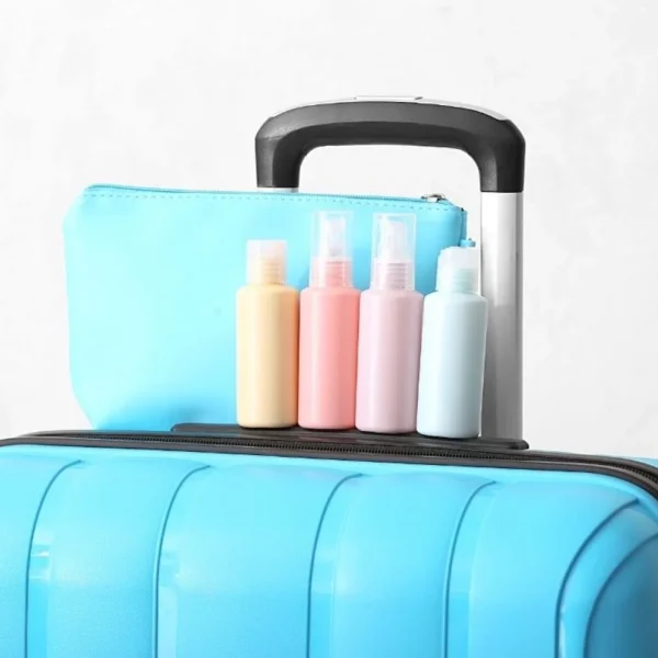 A light blue hard-shell carry-on suitcase with a matching toiletry bag and an assortment of pastel-colored travel-sized bottles for personal care products on top, against a neutral background.