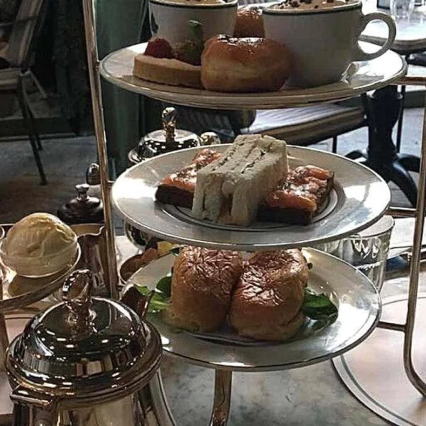 A sumptuous afternoon tea in England featuring an assortment of sandwiches, scones, and pastries, elegantly displayed on a tiered silver serving stand, ready to be enjoyed in a chic café setting.
