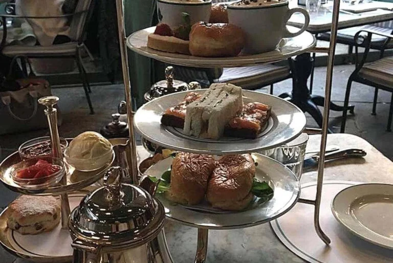 A sumptuous afternoon tea in England featuring an assortment of sandwiches, scones, and pastries, elegantly displayed on a tiered silver serving stand, ready to be enjoyed in a chic caf&eacute; setting.