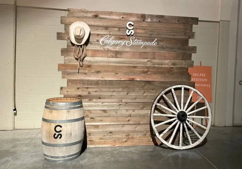 A rustic display with a large wooden Calgary Stampede sign, a barrel, and a wagon wheel, set up as a selfie station at the Calgary Stampede.