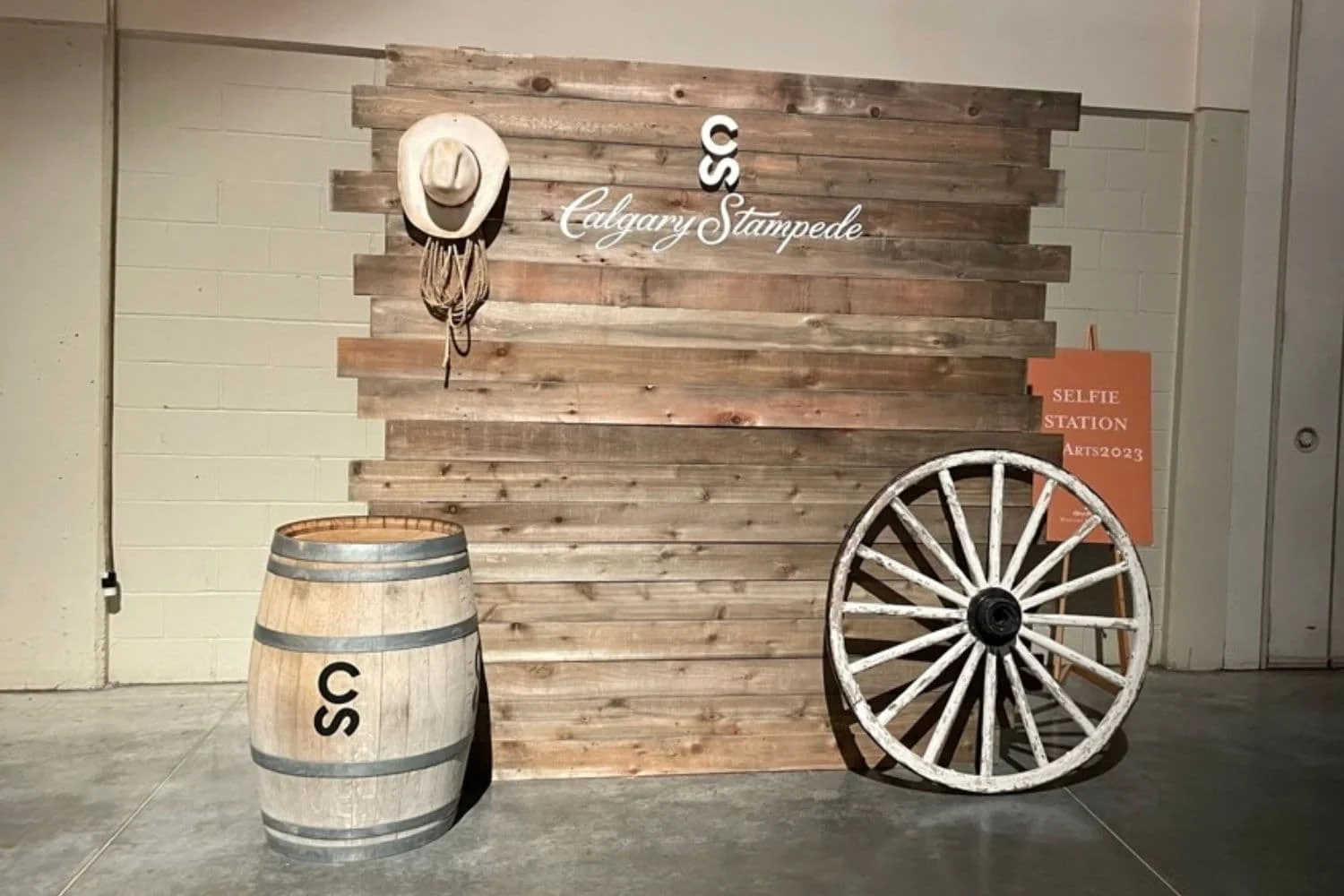 A rustic display with a large wooden Calgary Stampede sign, a barrel, and a wagon wheel, set up as a selfie station at the Calgary Stampede.