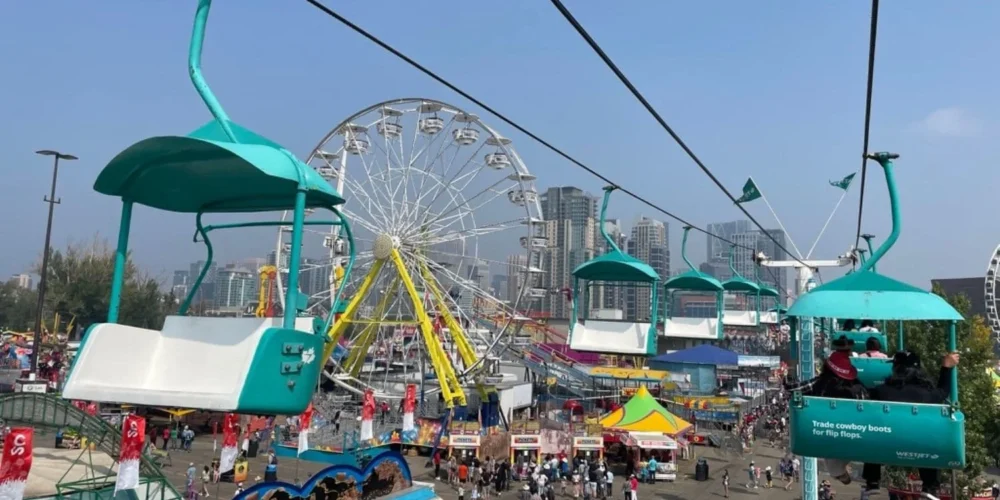 A view from a WestJet Skyride chair lift at Stampede Midway, looking down at the crowds and colorful rides below, including a Ferris wheel.
