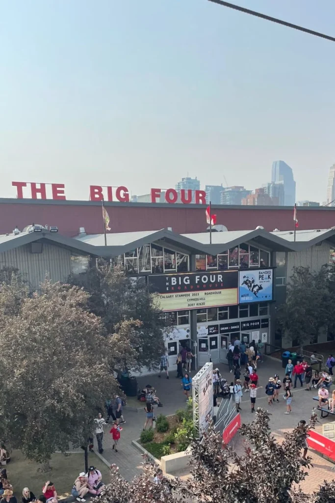 An aerial view of The Big Four Roadhouse at the Calgary Stampede. The large red "THE BIG FOUR" sign is prominently displayed on the roof, with people walking in and out of the venue below.
