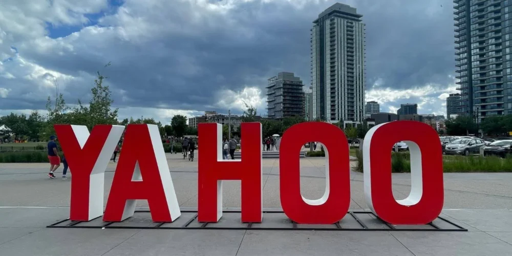 A large red "YAHOO" sign is displayed outdoors in a city plaza in Calgary, with modern high-rise buildings and a cloudy sky in the background.