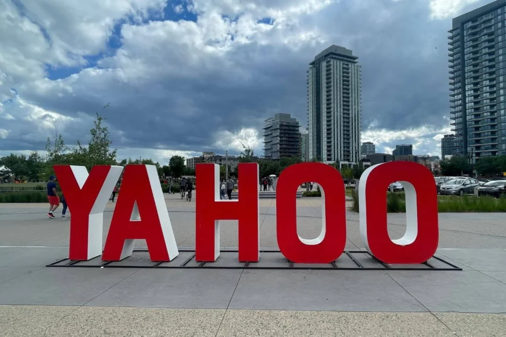 A large red "YAHOO" sign is displayed outdoors in a city plaza in Calgary, with modern high-rise buildings and a cloudy sky in the background.