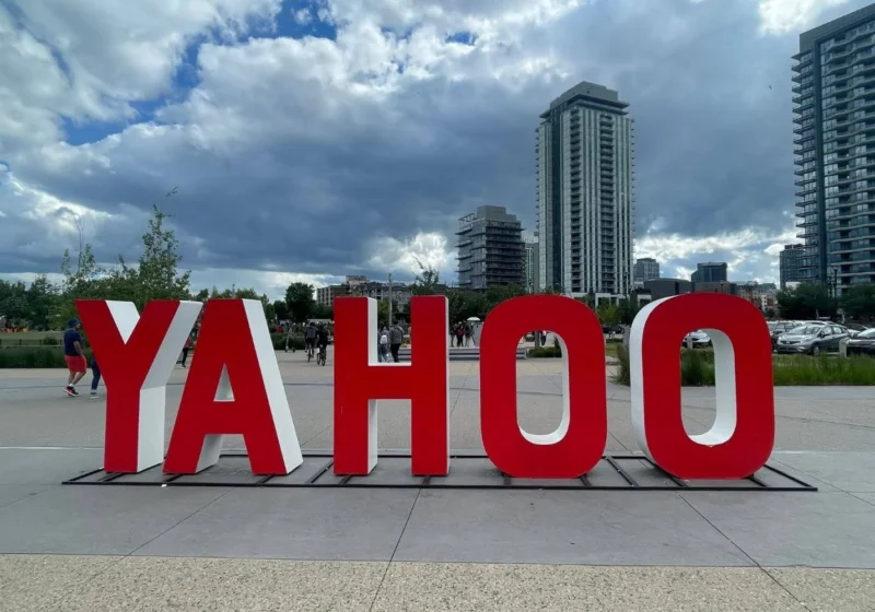 A large red "YAHOO" sign is displayed outdoors in a city plaza in Calgary, with modern high-rise buildings and a cloudy sky in the background.