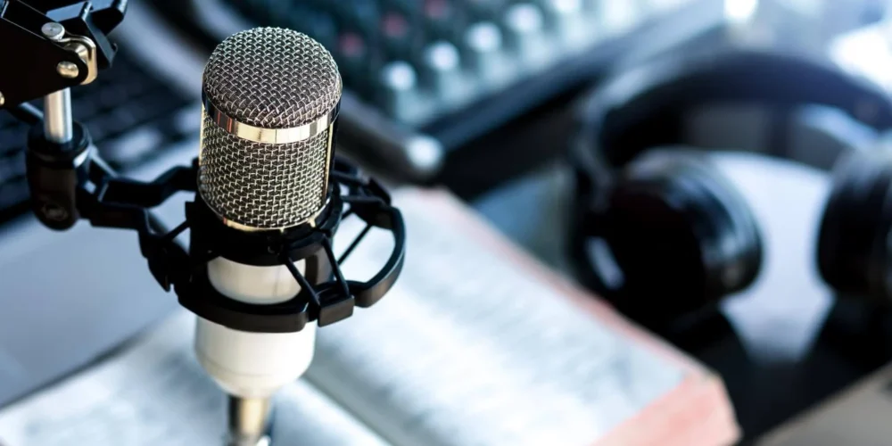 A close-up of a professional podcasting setup with a microphone, a pair of headphones, an open book, and a sound mixer in the background.