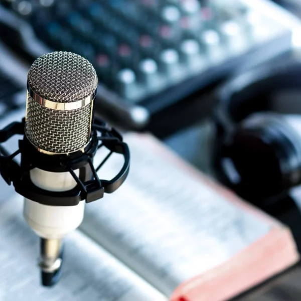 A close-up of a professional podcasting setup with a microphone, a pair of headphones, an open book, and a sound mixer in the background.