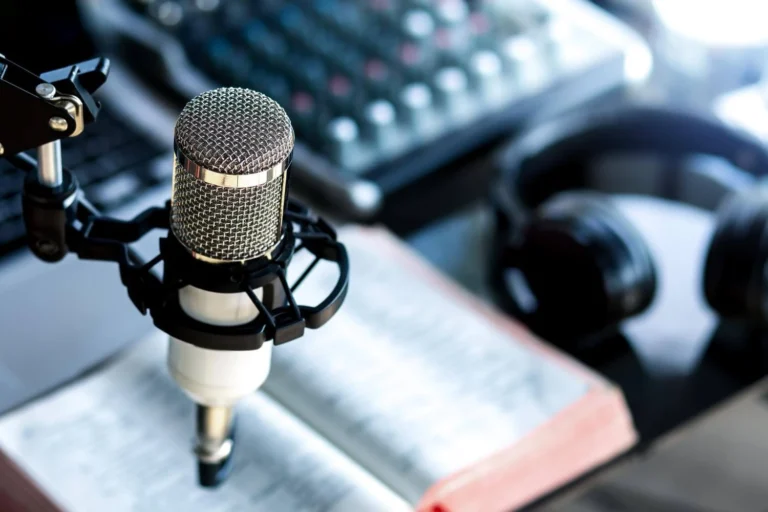 A close-up of a professional podcasting setup with a microphone, a pair of headphones, an open book, and a sound mixer in the background.