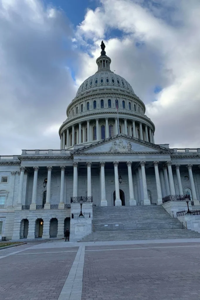 The U.S. Capitol building photographed from the side of its front steps on a cloudy day — symbolizing the fragile state of American democracy under Trump’s second term.