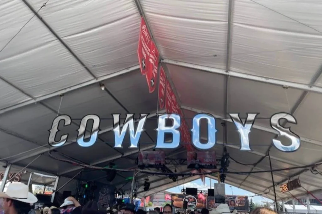 Reflective Cowboys sign hanging from the ceiling inside the packed Cowboys Music Festival tent during Calgary Stampede.