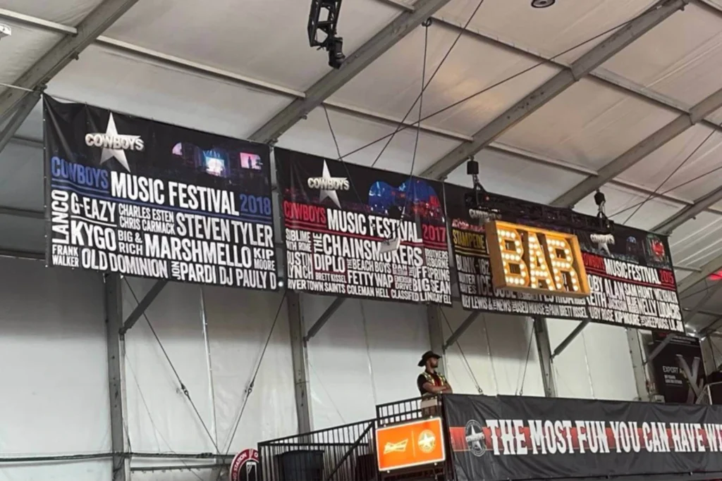 Cowboys Music Festival banner wall displaying past artist lineups with illuminated bar sign overhead at Calgary Stampede venue.