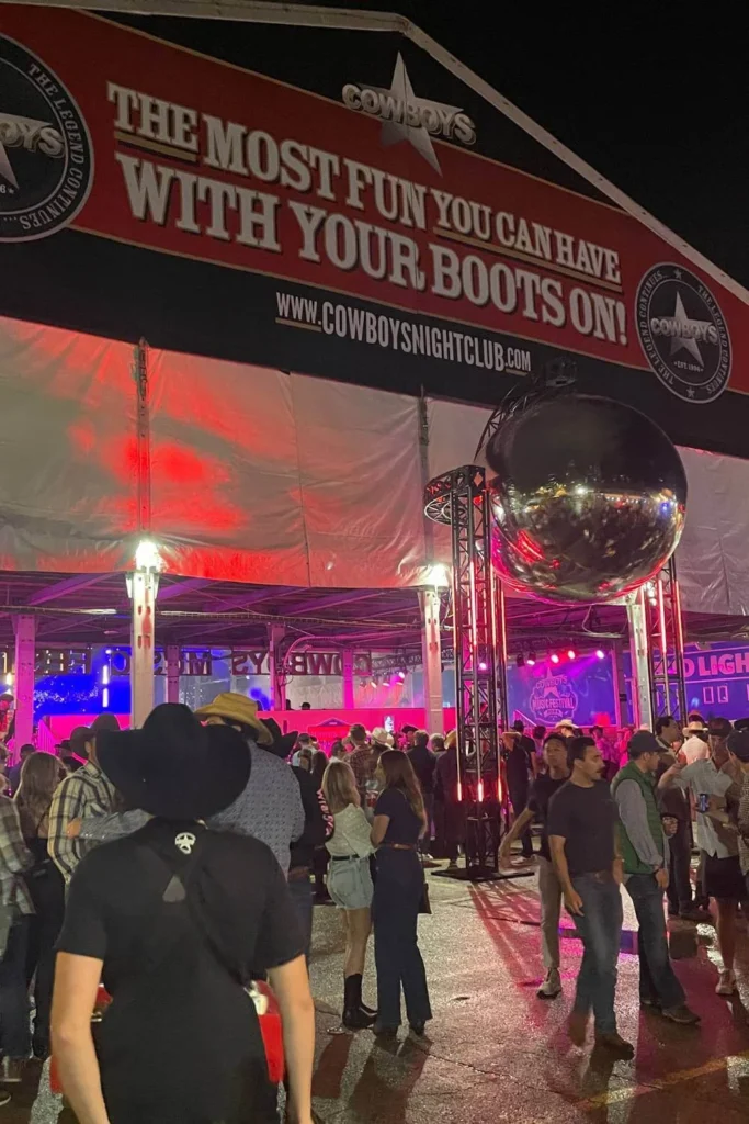 Nighttime crowd at the entrance of Cowboys Music Festival in Calgary during Stampede, with neon lights and signature western slogan banner overhead.
