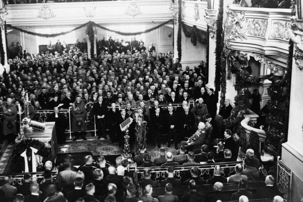 An official Nazi-era ceremony indoors, with military leaders and German officials gathered under ornate architecture during the rise of Hitler’s authoritarian regime.