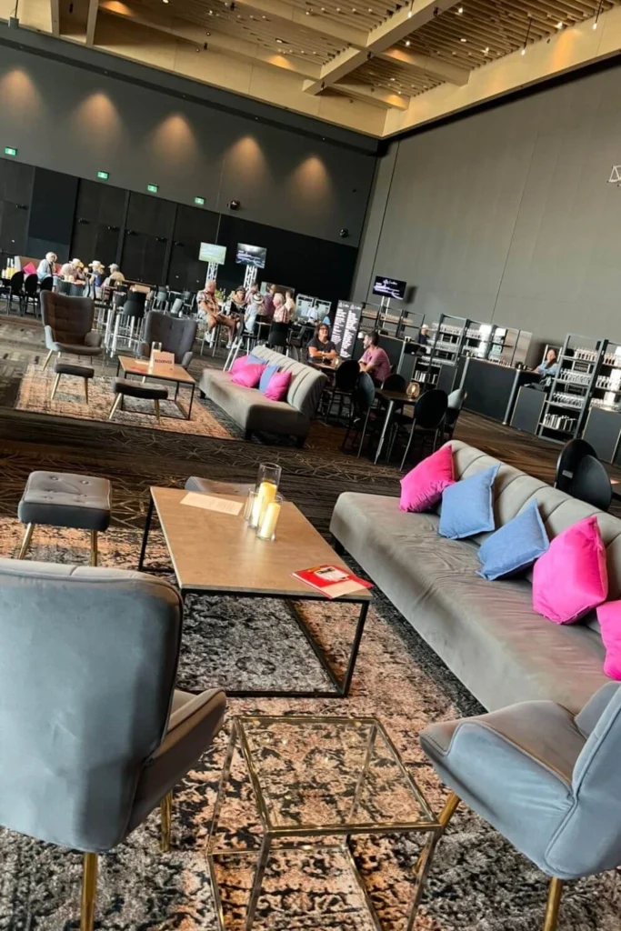 The Stampede Cellar at Calgary’s BMO Centre features a stylish setup with gray couches accented by bright pink and blue pillows, low tables with candles, and guests enjoying drinks at nearby high tables and the bar area.