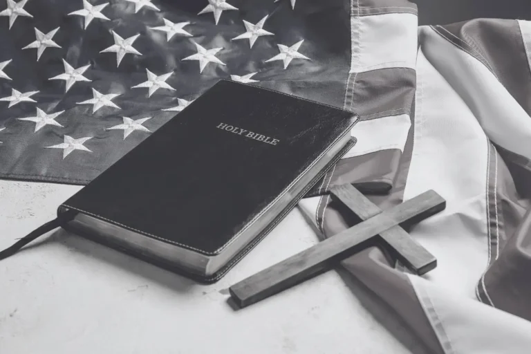 A bible and a simple wooden cross lay on an American flag symbolising Christian nationalism in America.