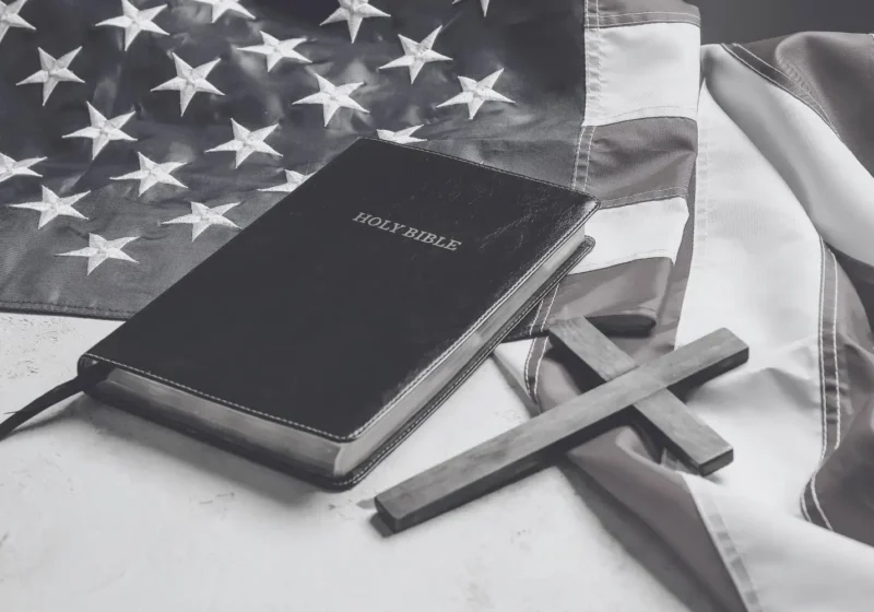 A bible and a simple wooden cross lay on an American flag symbolising Christian nationalism in America.