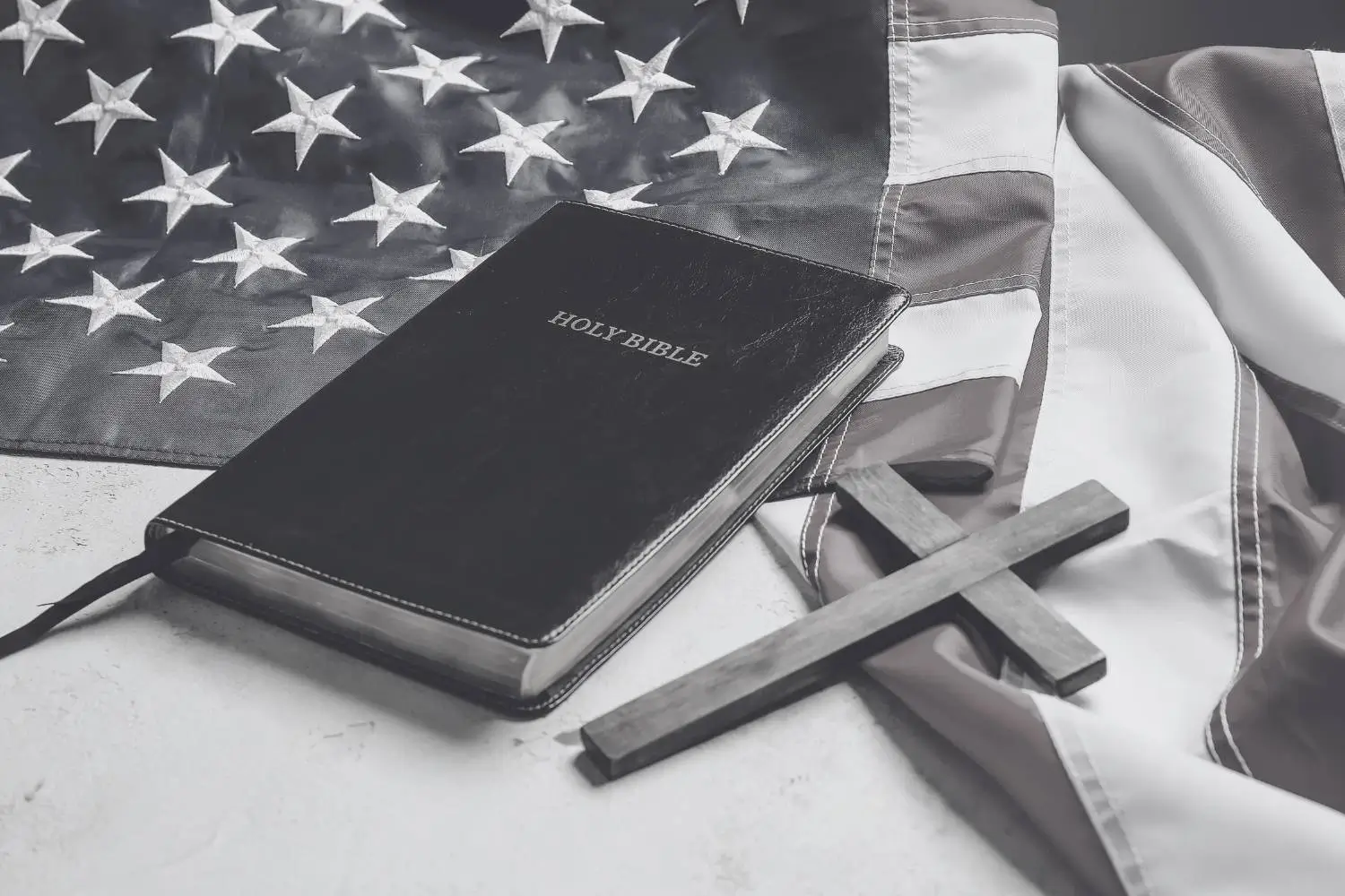 A bible and a simple wooden cross lay on an American flag symbolising Christian nationalism in America.