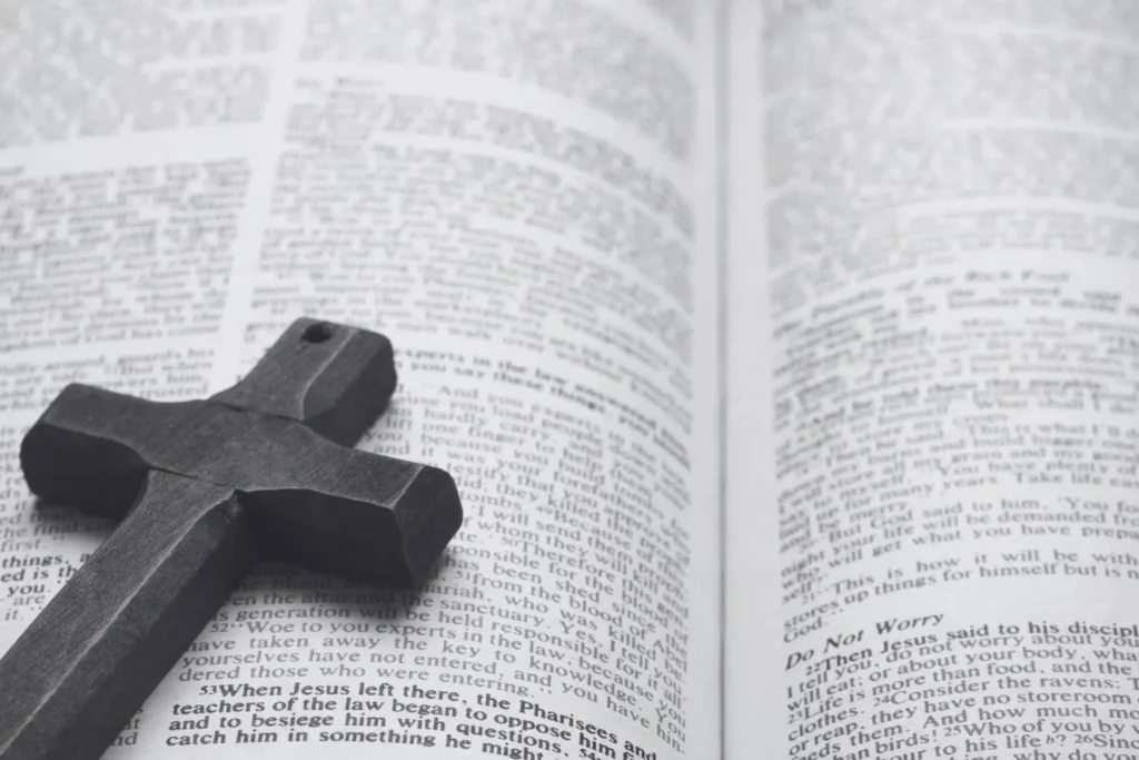 Black-and-white photo of a wooden cross resting on the open pages of a Bible, symbolizing Christian religious authority.