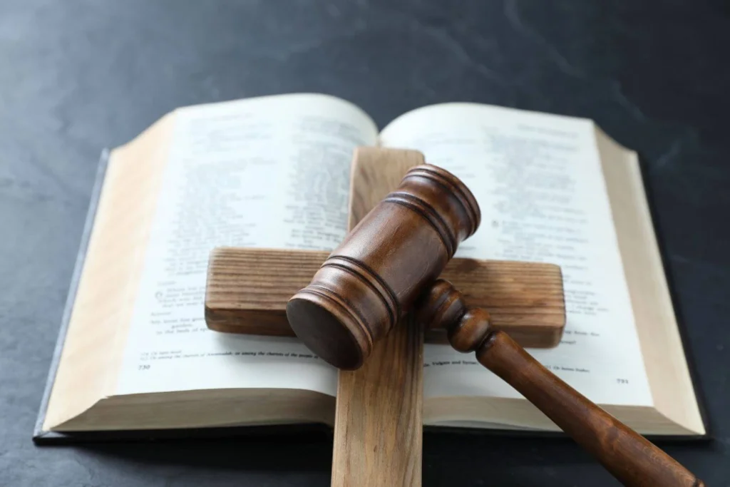 A wooden gavel resting on a cross laid across an open Bible, symbolizing the intersection of religion, law, and political power.