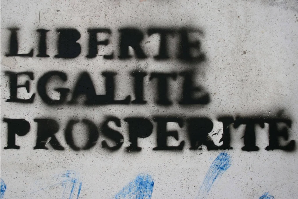Graffiti on a wall reading “Liberté, Égalité, Prospérité,” echoing the French Revolution call for liberty, equality, and resistance against oppression.