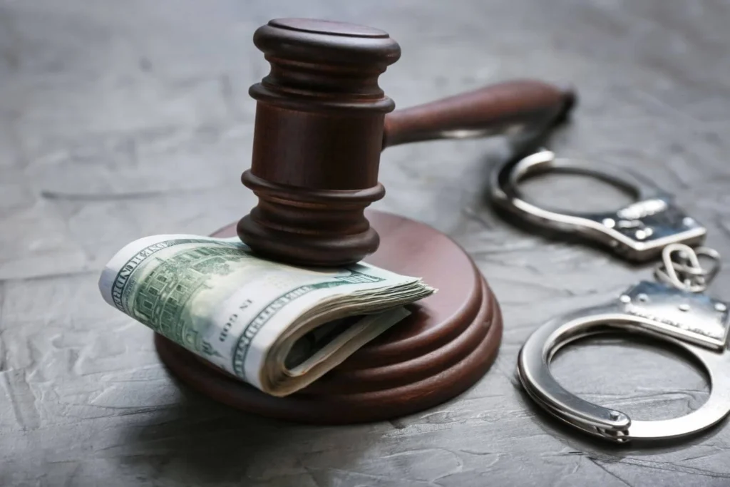A judge’s gavel resting on a roll of U.S. dollar bills beside handcuffs, symbolizing corruption, bribery, and abuse of power in politics and law.