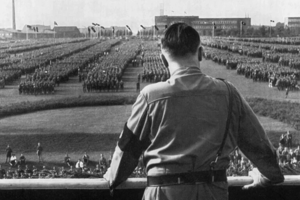 Black and white image of Adolf Hitler addressing a massive rally, symbolizing how fascist propaganda and mass obedience fueled authoritarian power in Nazi Germany.