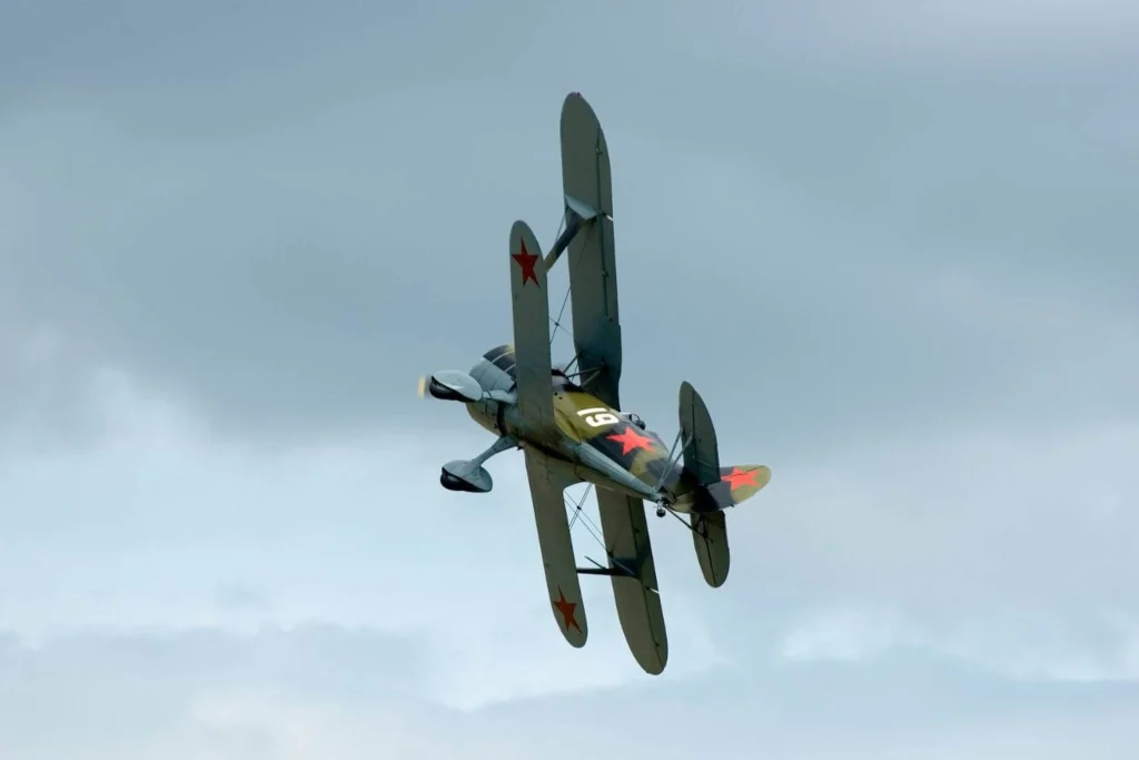 Vintage Soviet-era biplane with red star insignia banking in the sky during a World War II airshow at Duxford, England, representing Allied aviation history.