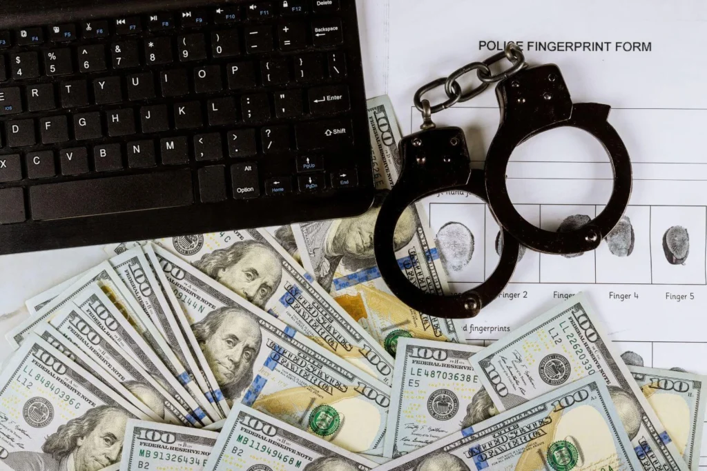 Keyboard, handcuffs, and hundred-dollar bills symbolizing criminal activities, corruption and abuses of power.