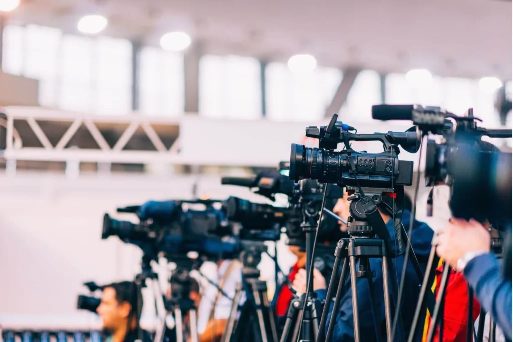 Row of professional news cameras recording a live press conference, symbolizing freedom of the press and independent media coverage.