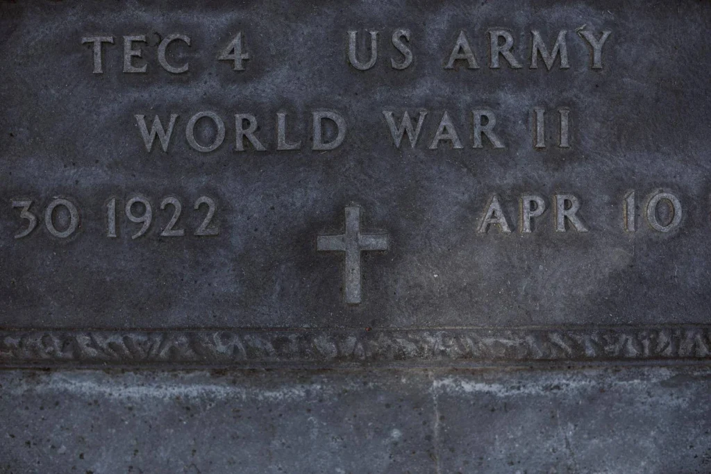 Close-up of a WWII US Army gravestone showing service details and a carved cross, representing the soldiers who fought against fascism.